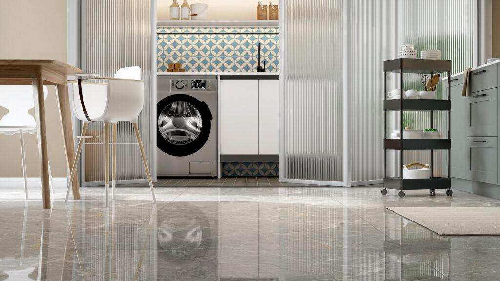 Sauberer grauer Marmorfliesenboden in zeitgenössischer Designküche mit Waschmaschine, Esstisch, Servierwagen und Kinderhochstuhl