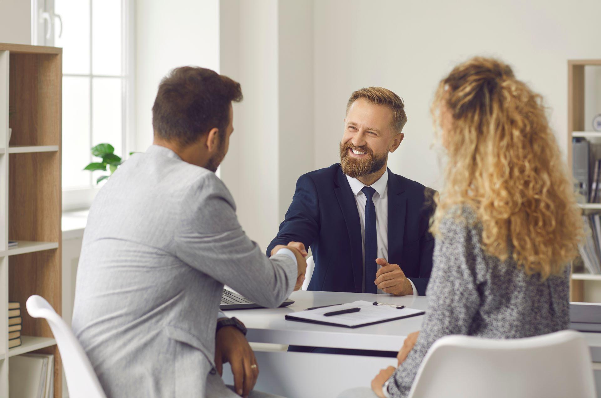 Ein freundlicher Anwalt, Immobilienmakler oder Finanzberater schüttelt einem jungen Paar die Hand. Ein Ehepaar, das ein Haus kaufen möchte, wendet sich an ein Immobilienbüro, einen Versicherungsmakler oder einen Bankangestellten. 