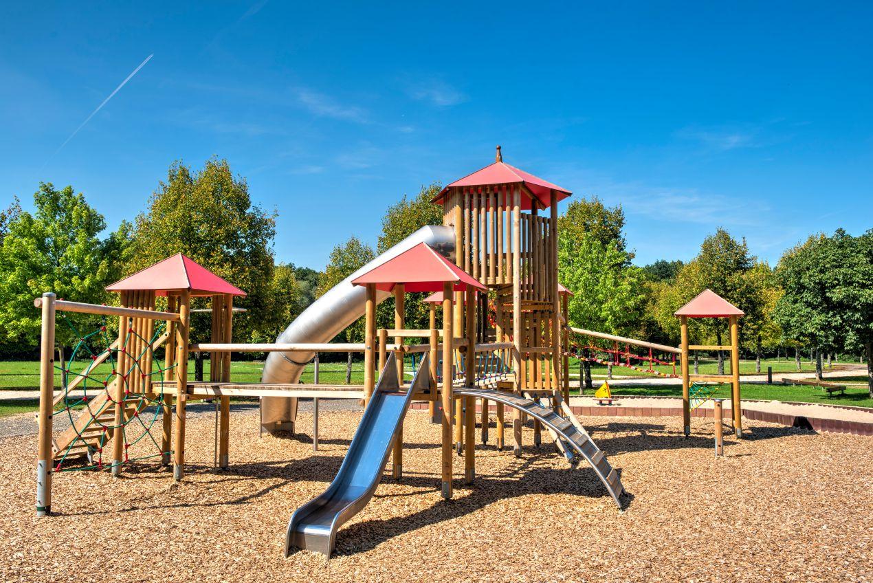 Ein weitläufiger Spielplatz mit hölzernen Klettertürmen, Rutschen und Kletterelementen. Langlebige Spielplatzgeräte für Kinder aller Altersgruppen.