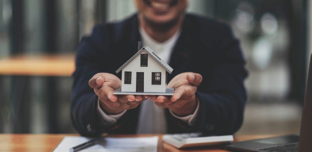 Hausmodell in ausgestreckten Händen | Baufinanzierung Köln