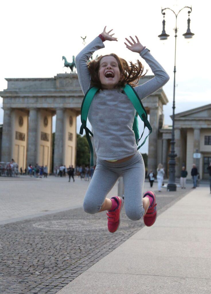 Fröhliches Schulkind springt mit Rucksack vor dem Brandenburger Tor – Symbolbild für bilinguale grundschule berlin