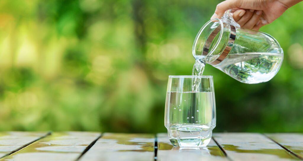 Glaskrug giesst Wasser in Glas im Garten | Wasserfilteranlage